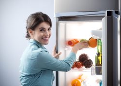 Young cheerful woman taking a green apple from refrigerator and smiling at camera.